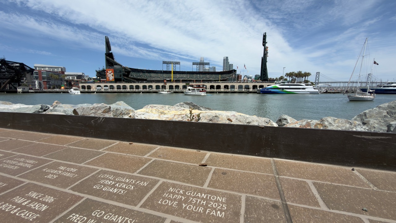 View across McCovey Cove toward Oracle Park, with boats and commemorative bricks in the foreground.